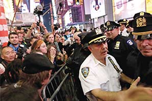 A big crowd of protesters and a group of policemen at opposite side of a road barrier.