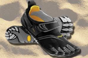 A pair of Black/gray/yellow FiveFingers shoes sitting on a background of sand.