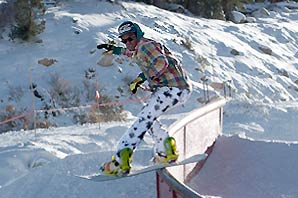 A snow boarder in snow gears gliding down the fence.