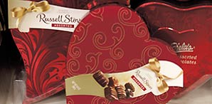 Several heart shaped red boxes of Russell Stover and Mrs. Field candies.