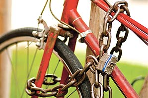 A red/silver/black bicycle with thick metal chain tied to a metal poll.