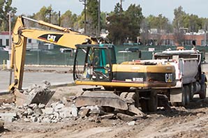 A CAT heavy earth breaking equipment breaking down cement on the ground inside green fenced area.