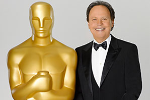 Comedian/actor Billy Crystal dressed in tuxedo standing beside a life size Oscar statue.