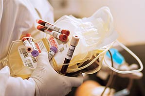 A medical personnel holding bags of empty blood bags and small tubes of blood samples.