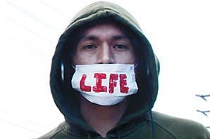 Juan Lerma wearing a hooded dark-green sweater with a white breathing mask over his mouth with the word LIFE in red print.