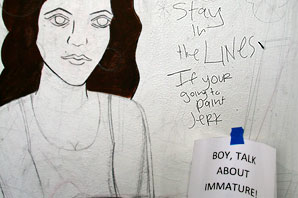 Graffiti of writing next to an art drawing of a women with long think hair reading Stay-in-the-LINES-If-your-going-to-paint-JeRK. Next to the graffiti is a printed note taped reading BOY,-TALK-ABOUT-IMMATURE!