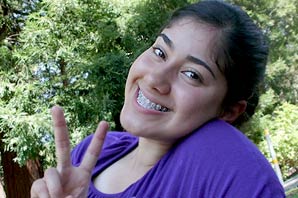 Close up portrait of Cristina Garcia smiling, with her fingers showing the Victory sign, and relaxing at the backyard.