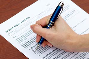 A student holding a ball point pen filling the USU-2012-13-AC-GRANT-APPLICATION form.