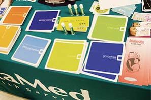 A table full of literature on common social and personal medical issues along with some give away like lip pump, sitting on top of a green table cloth imprinted with Alta-Med name and logo.