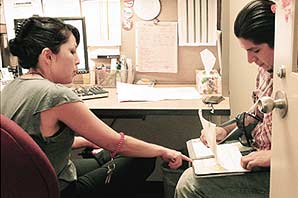 Counselor Sheri Blake and student Roger Vasquez sitting in her office while she is pointing to some paperwork Vasques is holding. On the wall are a series of letter size posting and charts and a computer monitor with keyboard.