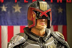 The Dredd character in his full Dredd armour standing in front of a old American flag.