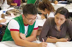 A tutor helping a student with her homework. On the background are several tables with other tutors and students.