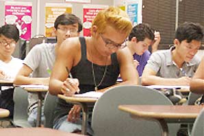 A room full of students sitting inside a classroom focus on writing or reading.