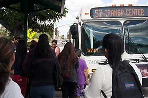 Three girls, 2 that are wearing backpacks, are about to go on the OCTA bus 57.