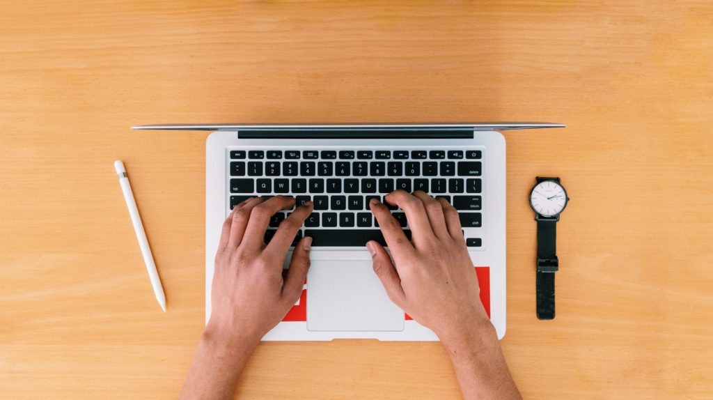 person using macbook pro on brown wooden table