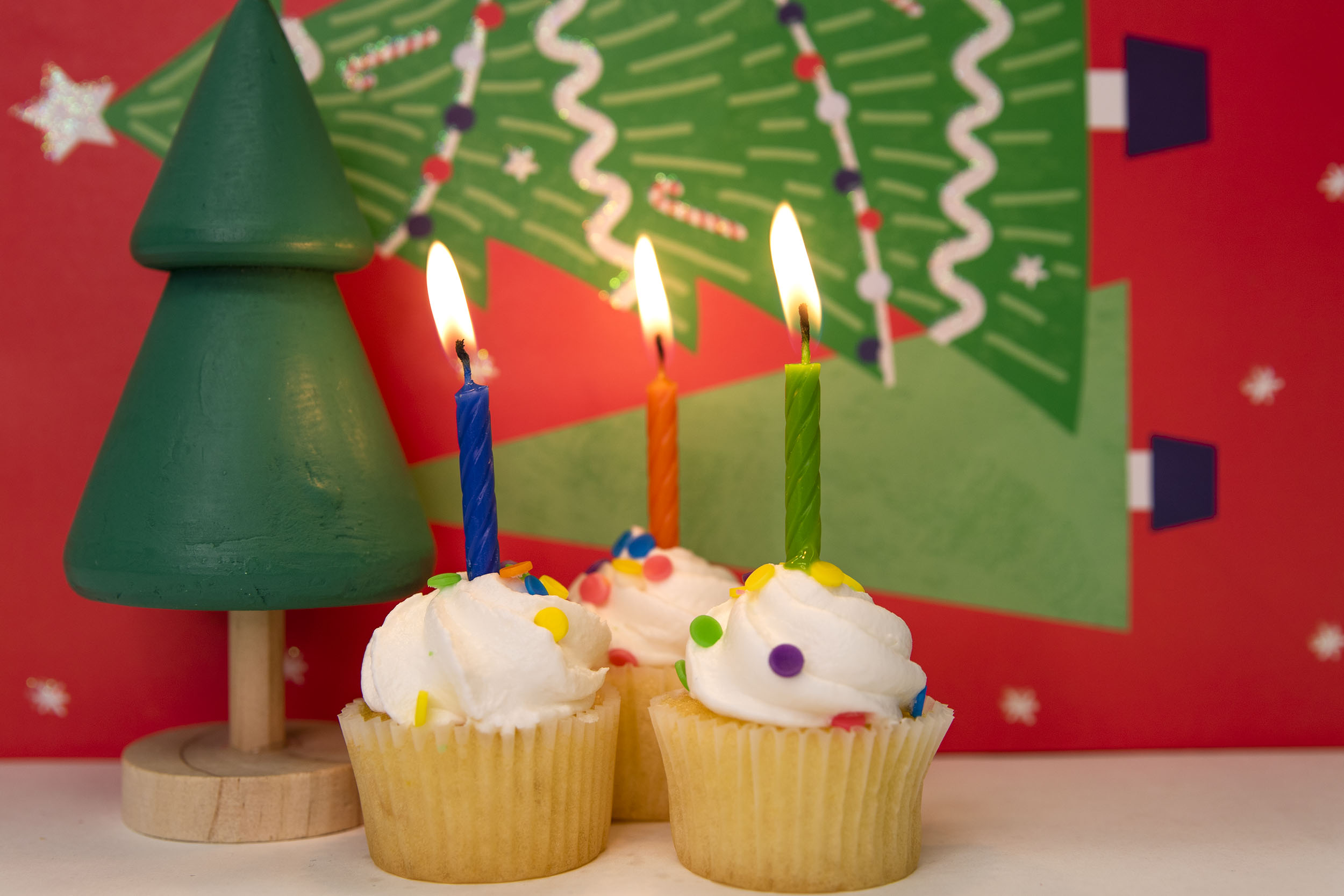 Photo of cupcakes with lit birthday candles and Christmas decorations