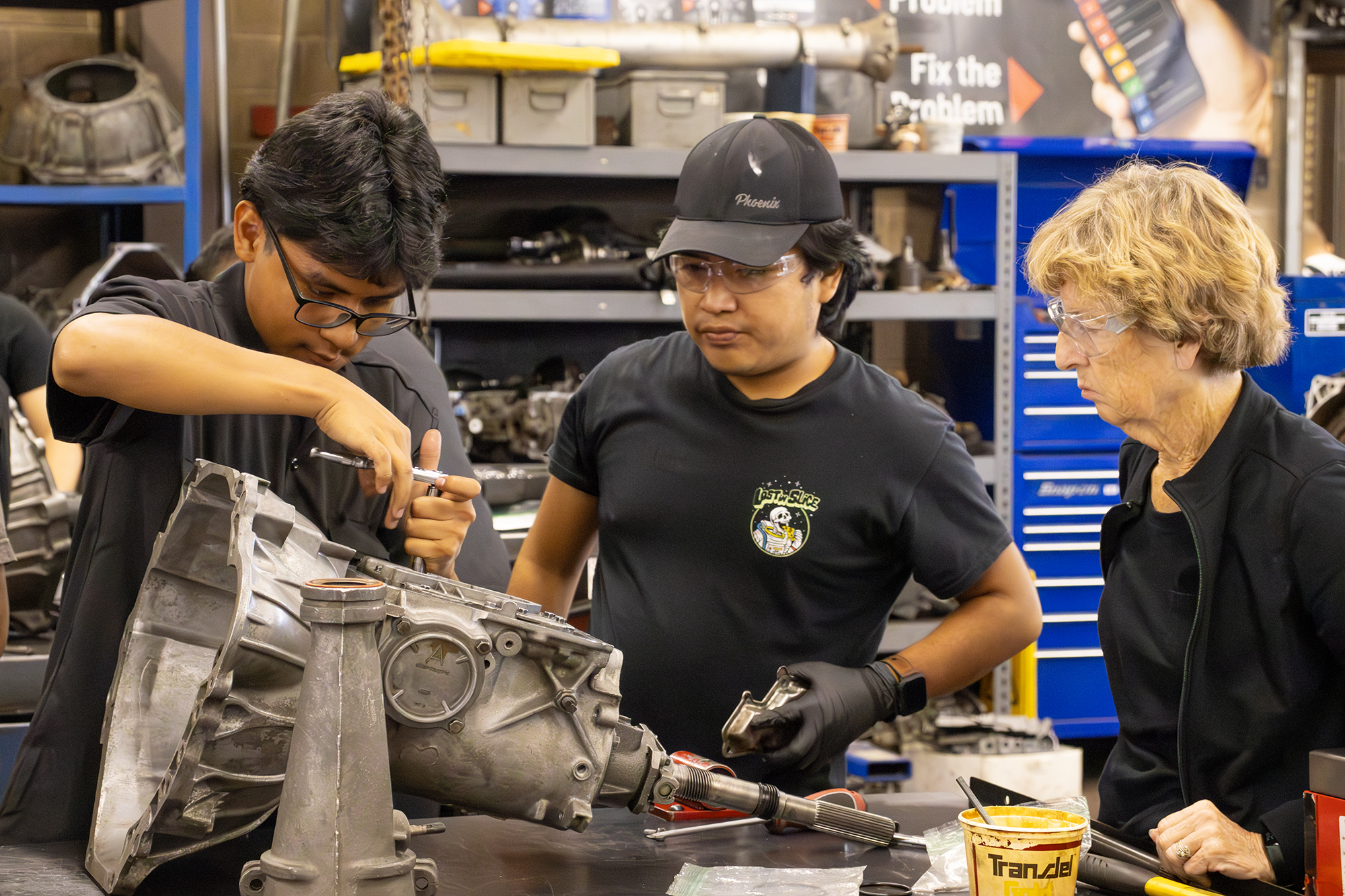 Three students learning to work on a transmission