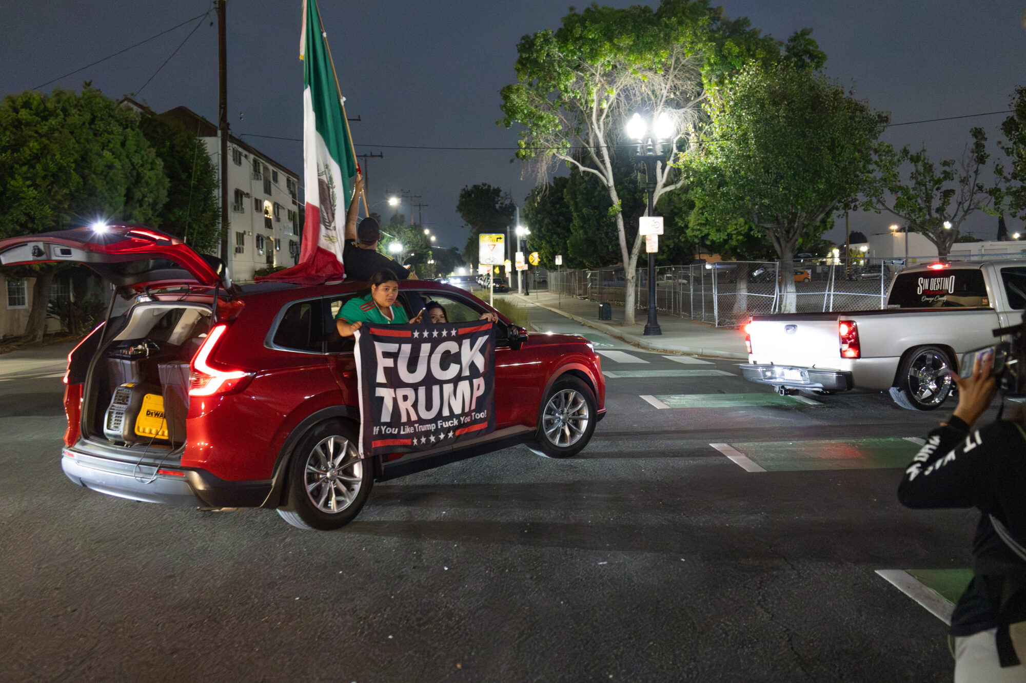 An SUV with a Mexican flag and a anti-Trump banner