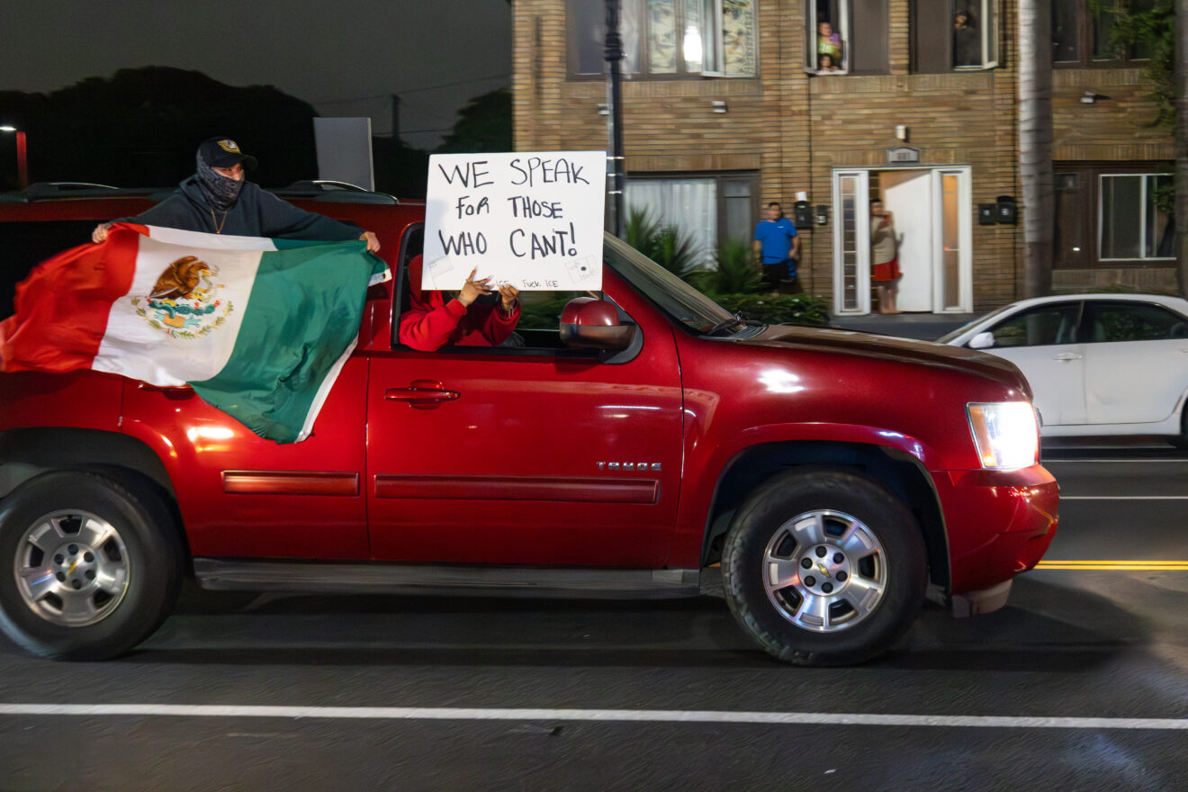 A red SUV driving with a Mexican flag hanging out the window