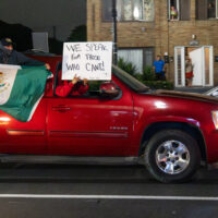 A red SUV driving with a Mexican flag hanging out the window