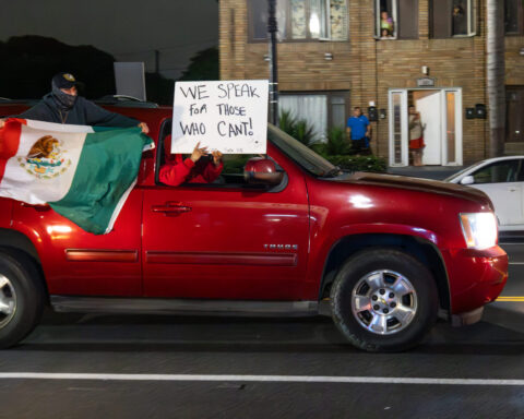 A red SUV driving with a Mexican flag hanging out the window