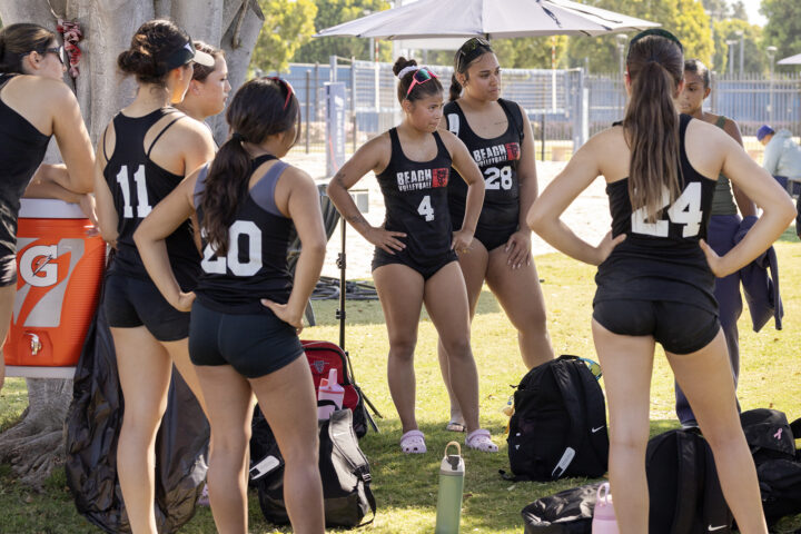 Women's beach volleyball team dressed in black tanks and shorts meet following 5-0 loss.