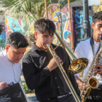 Four teenagers dressed in long sleeved shirts. One is playing the trombone and another a saxophone. The instruments of the other two boys aren't visible.