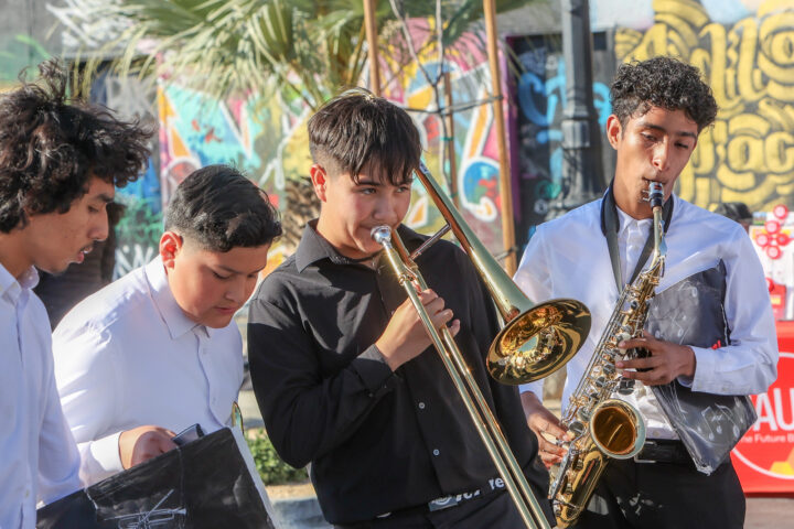 Four teenagers dressed in long sleeved shirts. One is playing the trombone and another a saxophone. The instruments of the other two boys aren't visible.