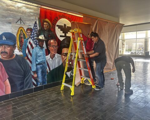 Three maintenece workers cover a colorful mural of Cesar Chavez and farmworkers on display in Santa Ana College.