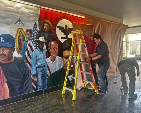 Three maintenece workers cover a colorful mural of Cesar Chavez and farmworkers on display in Santa Ana College.