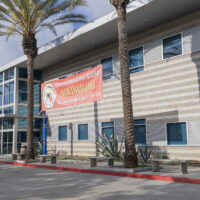 A building with a red banner between two palm trees advertising open enrollment for a local public charter high school.