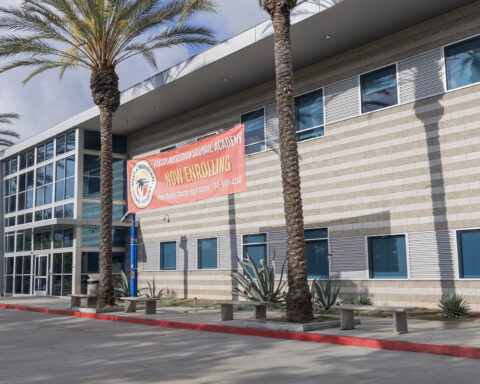 A building with a red banner between two palm trees advertising open enrollment for a local public charter high school.