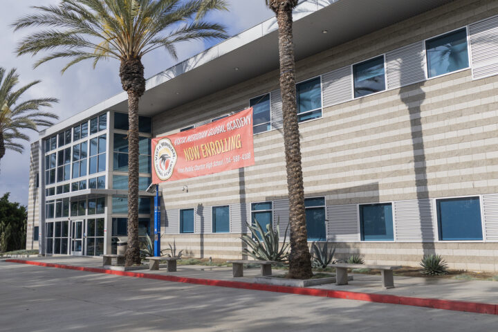 A building with a red banner between two palm trees advertising open enrollment for a local public charter high school.