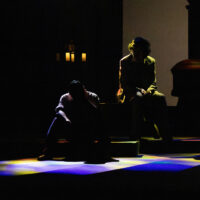 Two silhouettes on a stage with some colored lighting