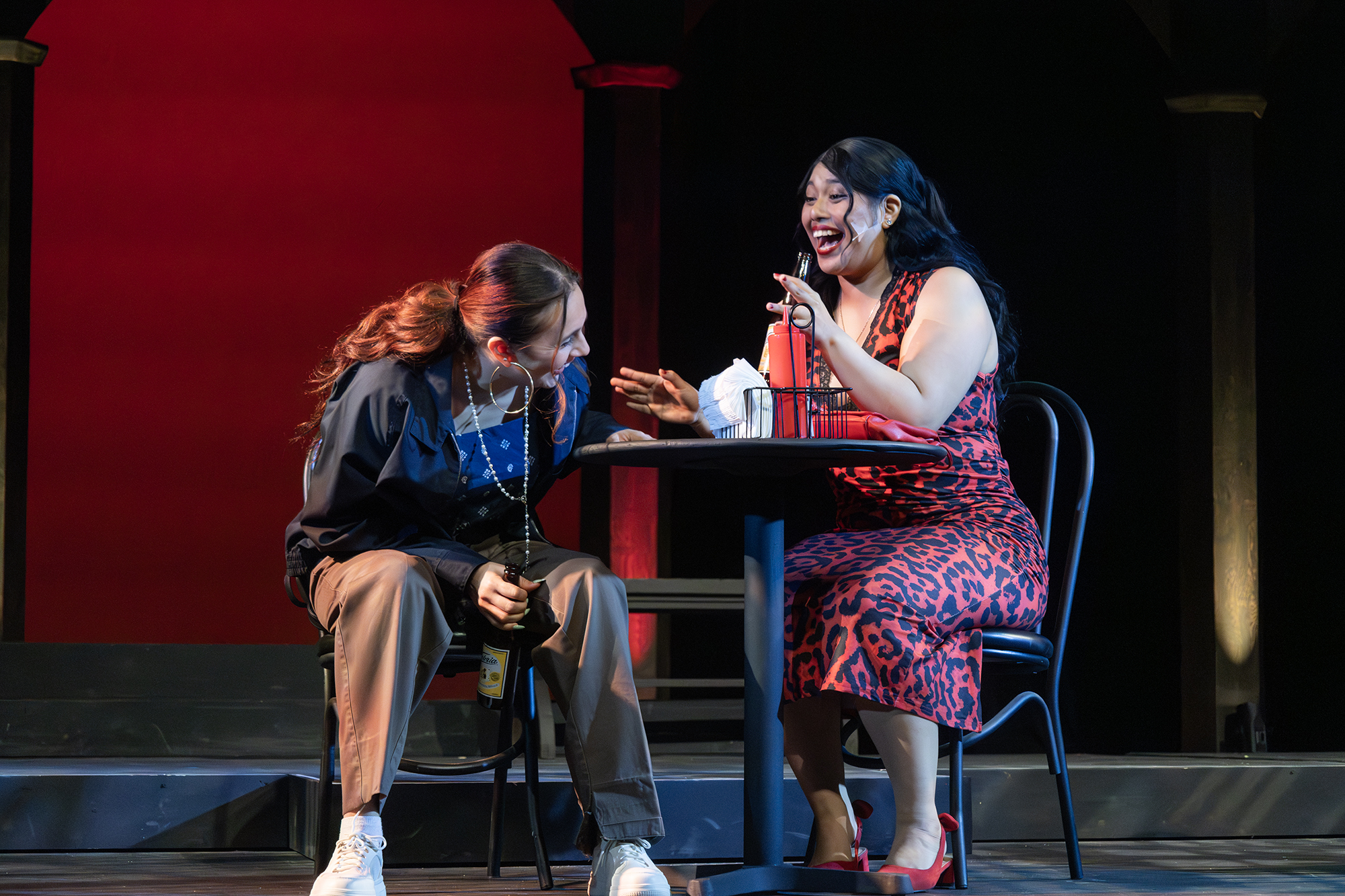 Two women sitting at a table laughing and drinking
