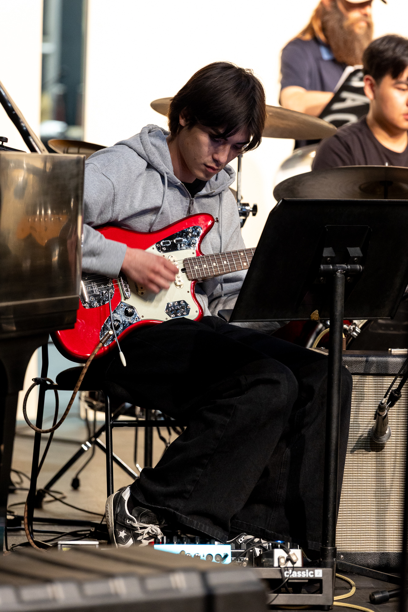 Young man plays a red and cream electric guitar during jazz ensemble rehearsal.